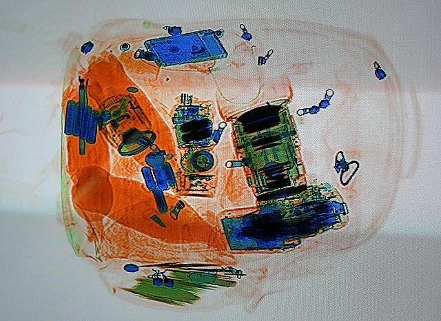 Rucksack bei der Gepäckdurchleuchtung. Software färbt das Bild nach Materialdichte: Organisches Material (Orange), Anorganische Materialien (Blau), Gemischte Materialien (Grün) 